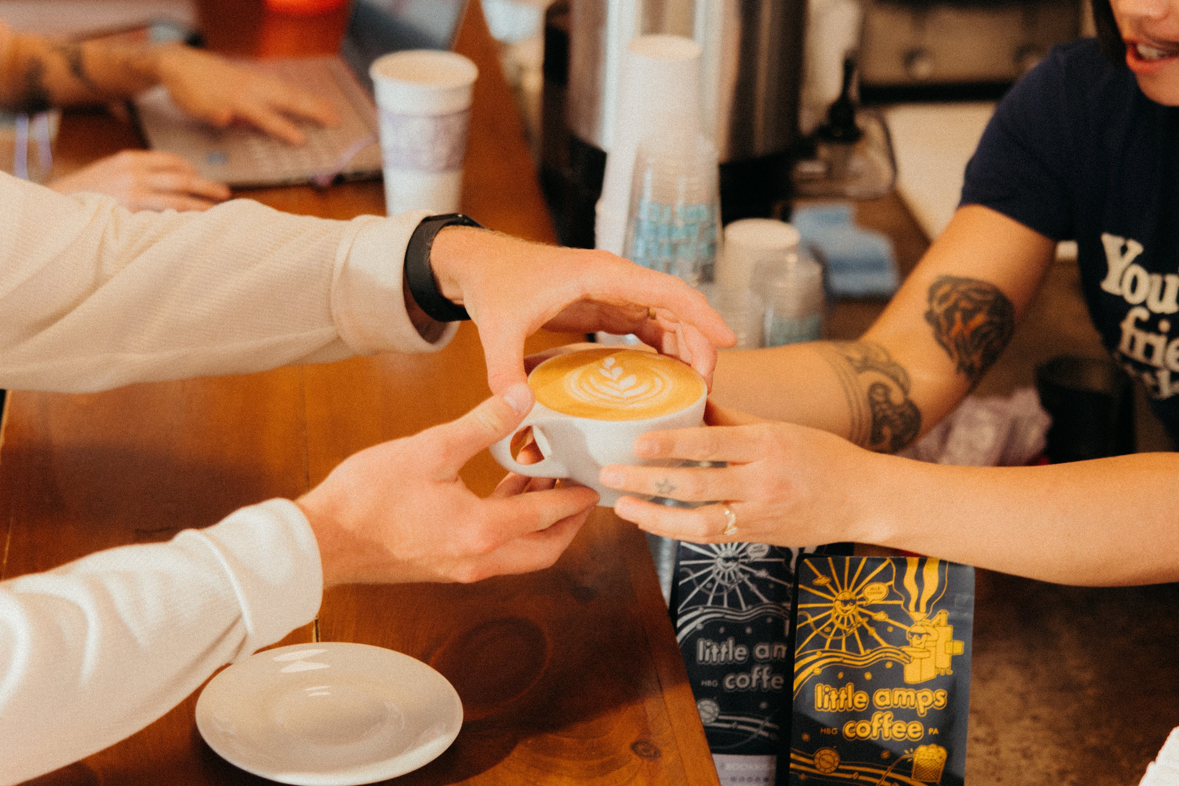 A person receiving a coffee drink in a mug with latte art from a Little Amps barista at the State Street store.