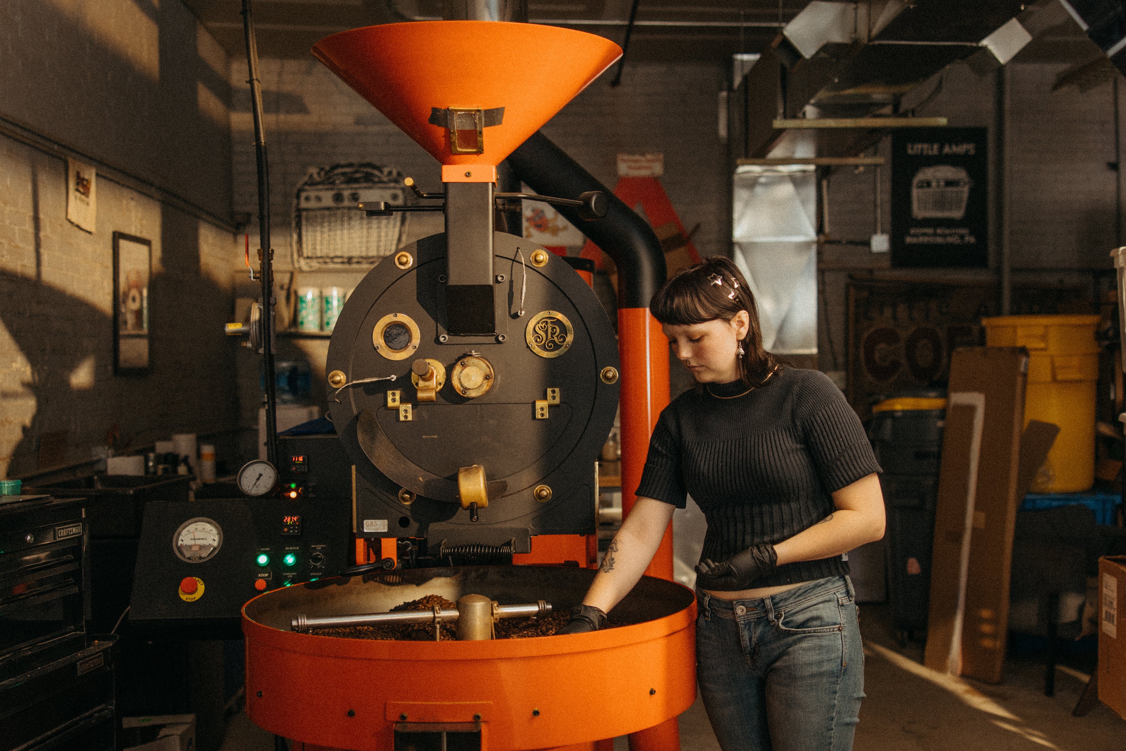 A person stands next to a roaster filled with coffee beans at Little Amps local roastery. 